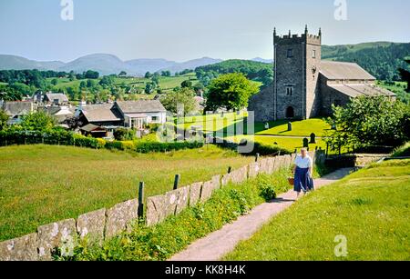 Villaggio inglese di hawkshead nel parco nazionale del distretto dei laghi, cumbria. donna camminando lungo il sentiero di San Michele è la chiesa parrocchiale Foto Stock