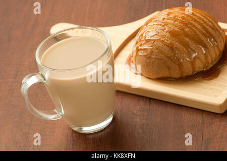 Pane spruzzata con miele su un piatto di legno e un bicchiere di latte shake Foto Stock