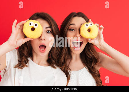 Due ragazze che fanno scherzi divertenti ed espressioni gioiose usando  fresco ciambelle al forno Foto stock - Alamy