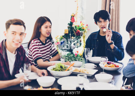 La cena con il gruppo asiatico di migliori amici gustando un drink serale mentre è seduto al tavolo da pranzo sulla cucina insieme,soft focus Foto Stock