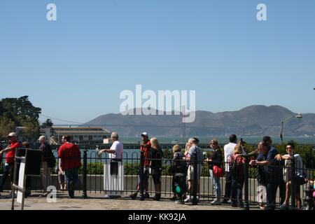 Una fotografia di un gruppo di persone in attesa in linea a bordo di una cabinovia Fisherman Wharf, la baia di San Francisco e il Golden Gate Bridge può essere visto in background, cavo auto sono state per la prima volta messo in servizio in città nel 1873, San Francisco, California, 2014. Foto Stock