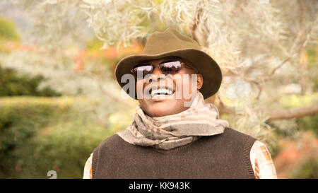 Bello e uomo felice godendo la vita all'aperto. Ritratto di sorridente uomo afro-americana all'aperto indossando un cappello e occhiali da sole escursioni, viaggi, o modello Foto Stock