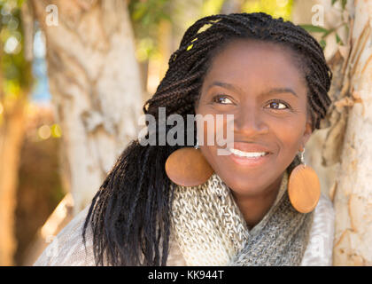 Bella donna afro-americana ritratto, sorridente in piedi appoggiata ad albero Foto Stock