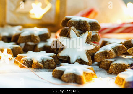 Tedesco tradizionali biscotti di Natale home cotto smaltato cannella stelle con dadi scintillanti luci garland candela candy canes sulla biancheria da letto bianca dello sfondo. Foto Stock