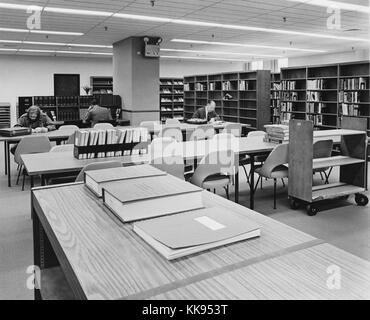 Fotografia in bianco e nero di una biblioteca area di lettura, con lunghi tavoli e scaffali di libri di riferimento e i lettori in background e la città di New York, New York, 1970. Dalla Biblioteca Pubblica di New York. Foto Stock