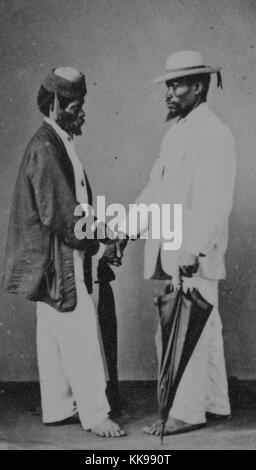 Una fotografia di due uomini non identificati stringono le mani, l'uomo a sinistra indossa una luce di colore camicia e pantaloni con un colore scuro camicia, l'uomo sulla destra indossa una luce colorata tuta e sta portando un ombrello, entrambi gli uomini sono a piedi nudi e di indossare cappelli, Brasile, 1900. Dalla Biblioteca Pubblica di New York. Foto Stock