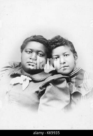 Un ritratto fotografico di due giovani donne, esse sono poste appoggiato gli uni verso gli altri con le loro teste toccando, la giovane donna sulla sinistra indossa un colore solido abito con un fiocco bianco al collo, la giovane donna sulla destra indossa un abito scuro modellato con luce strisce a colori, 1900. Dalla Biblioteca Pubblica di New York. Foto Stock