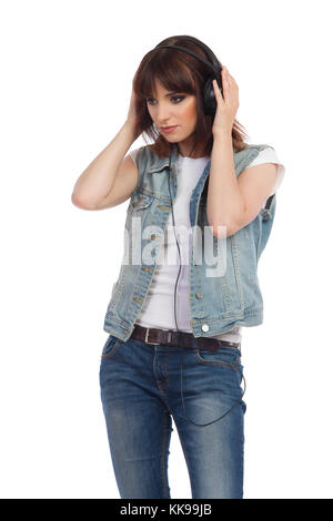 La giovane donna triste con il gilet senza bottone in jeans ascolta la musica con le cuffie e guarda lontano. Riprese in studio di tre quarti isolate sul bianco. Foto Stock