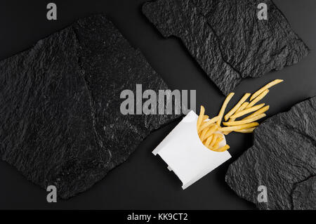 Patate fritte nella casella di colore bianco su uno sfondo di colore nero di lastre di pietra. La vista dall'alto Foto Stock