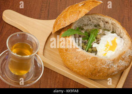 In casa la minestra di piselli e le uova in una ciotola di pane su un bordo e una tazza di tè verde Foto Stock
