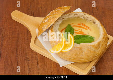 In casa minestra in crema guarnita con fette di limone in una ciotola di pane sulla scheda Foto Stock