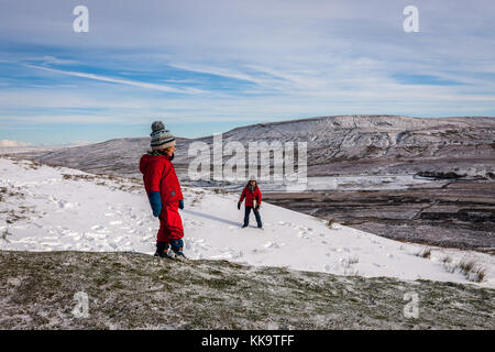 Bambini che giocano in inverno la neve su Pen Y Gand (694m), Yorkshire Dales Inghilterra Foto Stock