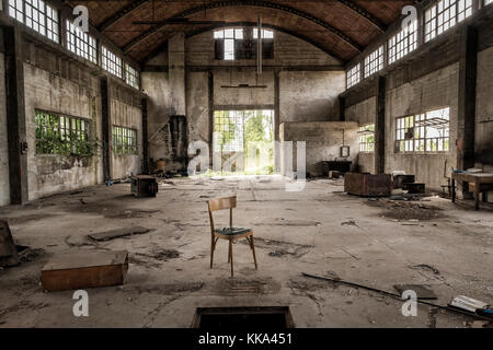 Fabbrica abbandonata (prospettiva centrale) con sedia in primo piano Foto Stock