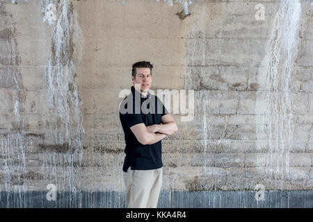 Un casualmente vestito uomo in piedi dietro un color beige parete. Tre quarti di lunghezza. Foto Stock