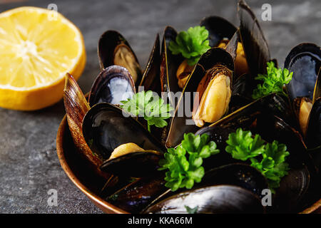 Cozze con erbe in un recipiente di rame. il pesce e il cibo presso la riva del mare francese. sfondo scuro Foto Stock