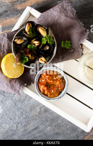 Cozze con erbe aromatiche in una ciotola con limone e vino bianco di una tavola di legno. Il pesce e il cibo presso la riva del mare francese. sfondo scuro Foto Stock