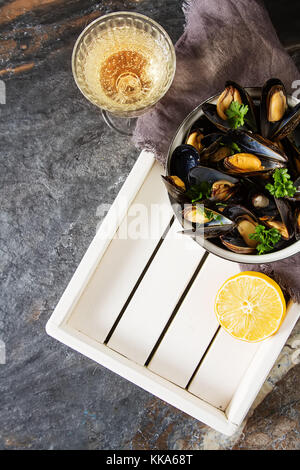 Cozze con erbe aromatiche in una ciotola con limone e vino bianco di una tavola di legno. Il pesce e il cibo presso la riva del mare francese. sfondo scuro Foto Stock