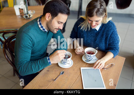 Giovane coppia attraente utilizzando tablet in coffee shop Foto Stock