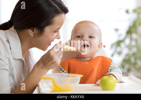 Madre che nutre il suo bambino con cucchiaio. madre dando cibo sano per il suo adorabile bambino a casa Foto Stock