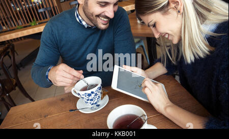 Giovane coppia attraente utilizzando tablet in coffee shop Foto Stock