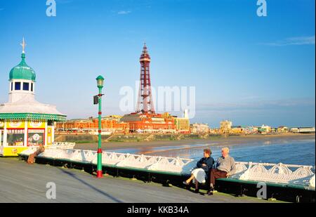 Coppia anziana seduta sul molo nord di Blackpool Beach con la Blackpool Tower alle spalle. Lancashire, Inghilterra, Regno Unito. Estate Foto Stock