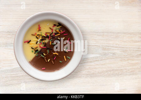 Vaniglia e cioccolato cremoso dessert orned con multicolore di caramelle sul tavolo di legno sfondo Foto Stock