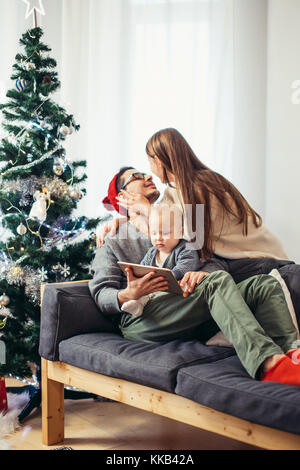 Famiglia seduto in soggiorno divertendosi con tablet pc che Babbo Natale ha portato Foto Stock