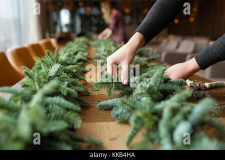 Fioraio al lavoro: donna mani rendendo le decorazioni di Natale ghirlanda di fir. Felice anno nuovo cena festa Foto Stock