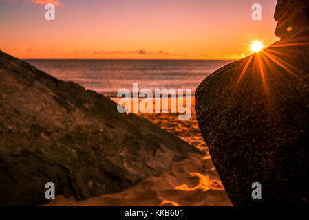 Bellissima spiaggia sfondo con il sole che sorge dietro le rocce. adorabile, morbidi colori di mattina Foto Stock