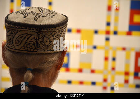 Grigio-dai capelli uomo con coda di cavallo che indossa pill box hat guardando Piet Mondrian 'Broadway Boogie Woogie" al MoMA di New York City Foto Stock