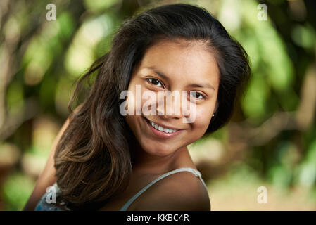 Attraente sorridente giovane donna ispanica headshot ritratto su sfondo naturale senza trucco Foto Stock