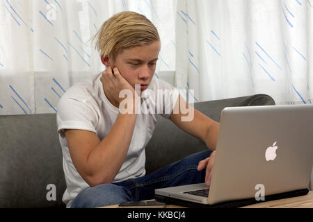 Adolescente maschio su un lettino usando il suo MacBook Pro Apple per i compiti a casa mantenendo i suoi amici aggiornati su reti sociali Foto Stock