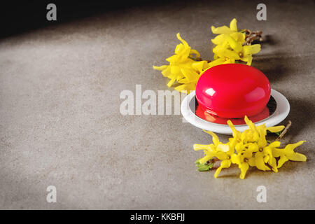 Mousse di moda la torta con una glassa a specchio decorato con fiori di primavera. sfondo scuro. Foto Stock
