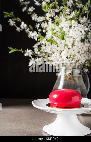 Mousse di moda la torta con una glassa a specchio decorato con fiori di primavera. sfondo scuro. Foto Stock