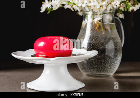 Mousse di moda la torta con una glassa a specchio decorato con fiori di primavera. sfondo scuro. Foto Stock