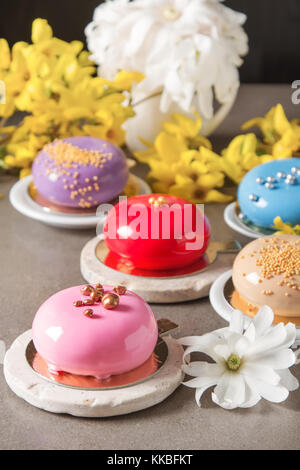 Mousse di moda la torta con una glassa a specchio decorato con fiori di primavera. sfondo scuro. Foto Stock