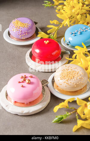 Mousse di moda la torta con una glassa a specchio decorato con fiori di primavera. sfondo scuro. Foto Stock