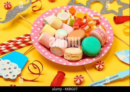 Parte colorata, caramelle e coriandoli su sfondo giallo top view mockup Foto Stock