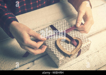 Donna incarto di un regalo per diletto. la legatura di un nastro in prua con cuore in legno Arredamento Foto Stock