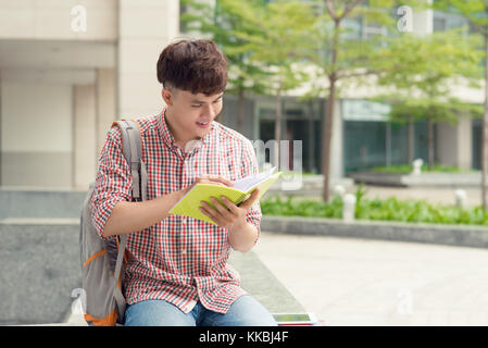 Giovane uomo asiatico con zaino la lettura di un libro Foto Stock