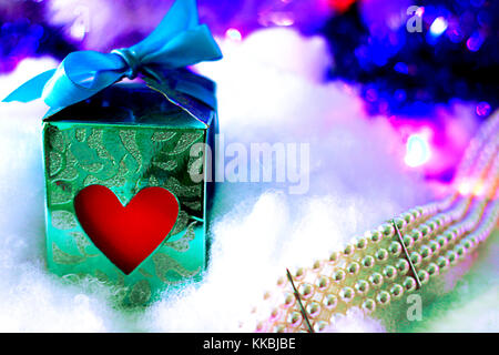 Confezione regalo con cuore rosso e blu ribbon su morbido innevate sullo sfondo bokeh di fondo con gioielli perla. Natale, Capodanno o modello di San Valentino con spazio per t Foto Stock