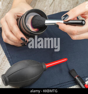 Il fotografo pulisce la lente di polvere su di un tavolo di legno. close-up. illuminazione da studio Foto Stock