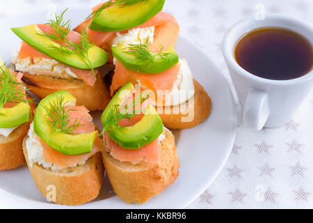 La bruschetta, snack panini con formaggio bianco, salmone affumicato e pezzi di avocado decorata da aneto. Foto Stock