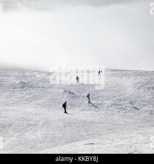 Gli sciatori e gli snowboarder in discesa su pendio nevoso e alla luce del sole nel cielo di nebbia a sun inverno mattina. montagne del Caucaso, Georgia, regione gudauri. Foto Stock