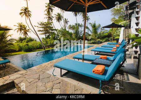 Piscina e sedie a sdraio di fronte ad un giardino e mare nella boutique hotel. Foto Stock