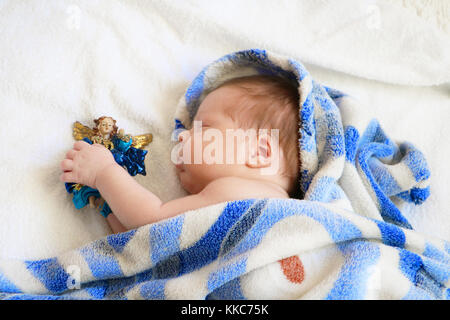 Carino neonato dormire in coperta blu con la figura di angelo nelle mani su sfondo bianco. Foto Stock