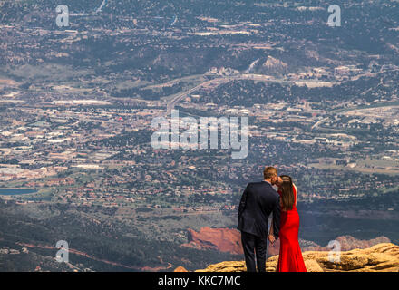 Giovane uomo in un abito nero e una giovane donna in un lungo abito rosso stand sulla sommità del Pikes Peak, Colorado, guardando in giù a valle al di sotto Foto Stock