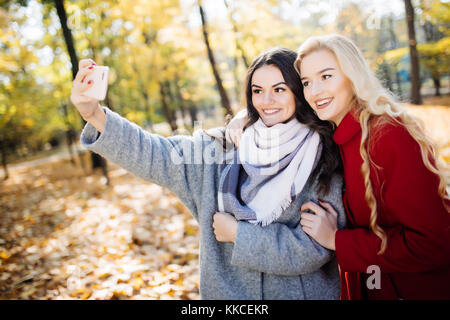 Felice di due ragazze adolescenti prendendo un selfie sullo smartphone, all'aperto in autunno. Foto Stock