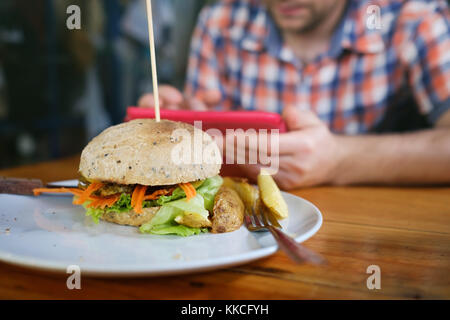 Veggie patata dolce burger con verdure fresche servita su piastra bianca. sfocato uomo caucasico seduta sullo sfondo Foto Stock