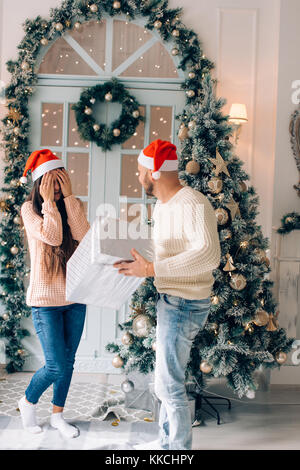 Coppia con presente sorridente abbraccia delicatamente a luci di Natale Foto Stock